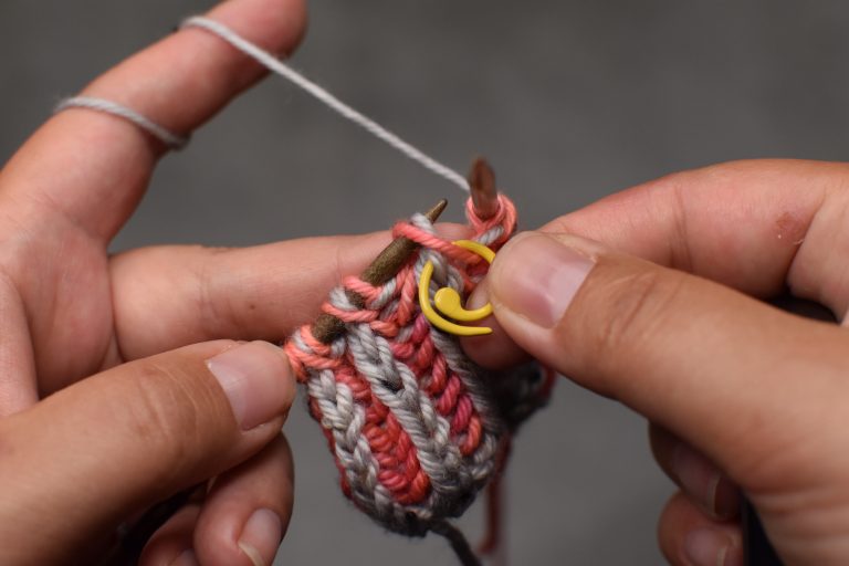 Schritt 3: Die Mittelmasche (samt dem Umschlag) auf einen entfernbaren Maschenmarkierer fädeln...